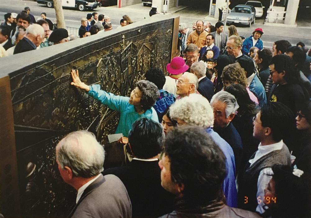 Asawa and large crowd gathered awround sculpture wall