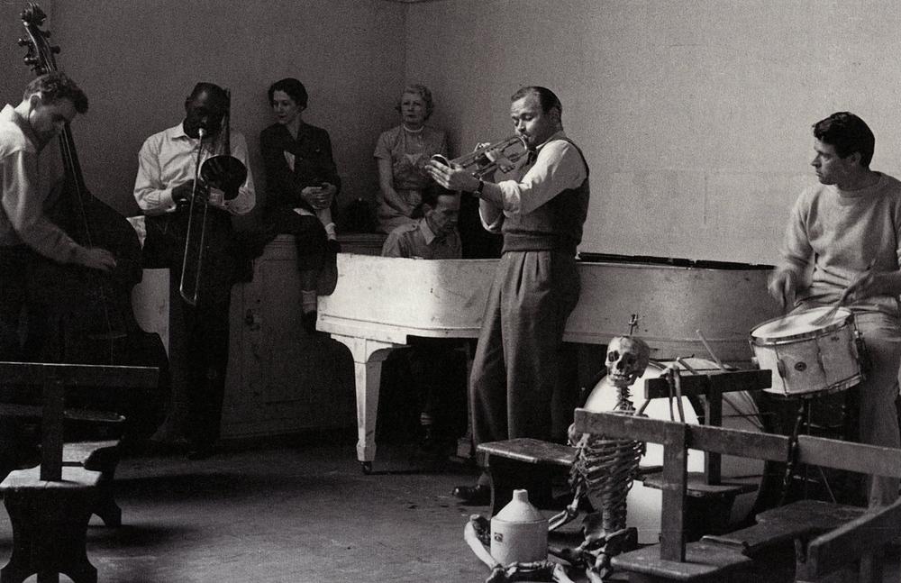 jazz band musicians playing music in open room with onlookers sitting amongst them