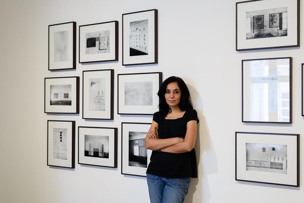 Artist leaning on white gallery wall in front of their work