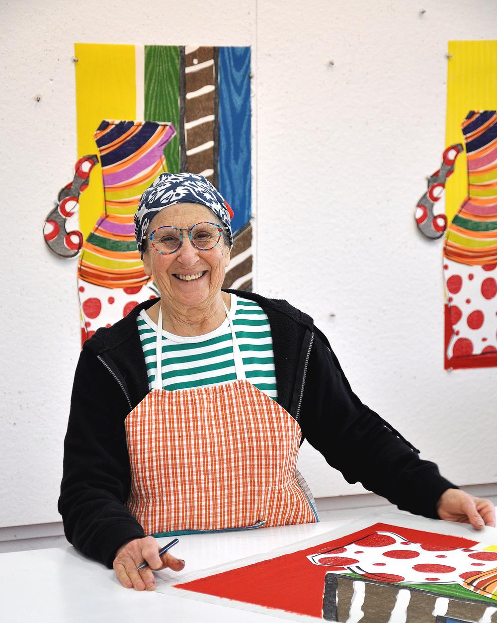 artist working in their studio with brightliy colored pieces hanging in her studio